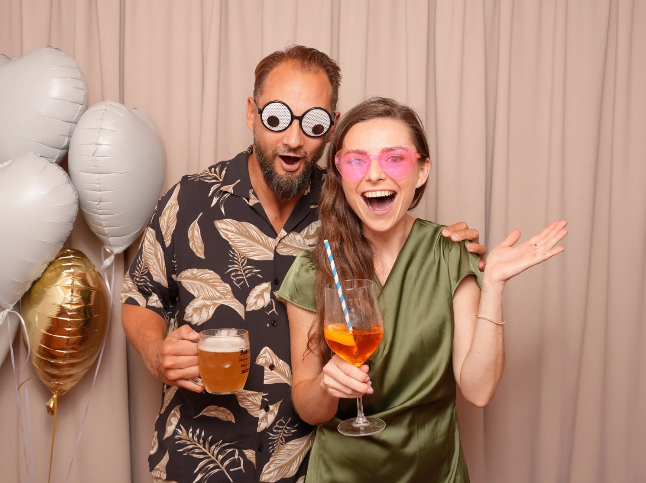 Svatební hosté s drinky a balónky zachyceni fotobudkou během párty.